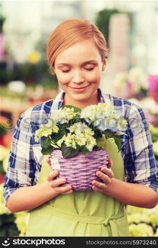 people, gardening and profession concept - happy woman or gardener smelling flowers in greenhouse