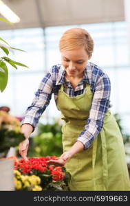 people, gardening and profession concept - happy woman or gardener taking care of flowers in greenhouse