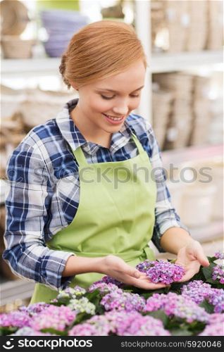 people, gardening and profession concept - happy woman or gardener taking care of flowers in greenhouse