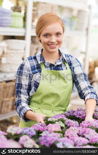 people, gardening and profession concept - happy woman or gardener taking care of flowers in greenhouse