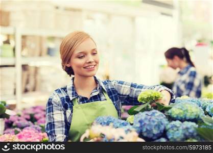 people, gardening and profession concept - happy woman or gardener taking care of flowers in greenhouse