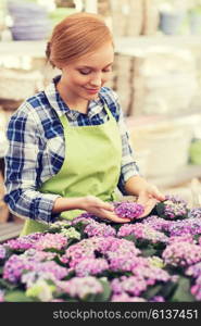 people, gardening and profession concept - happy woman or gardener taking care of flowers in greenhouse