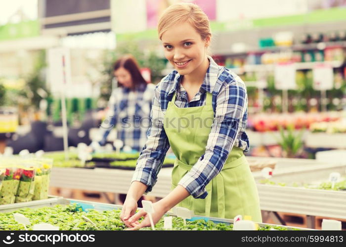 people, gardening and profession concept - happy woman or gardener taking care of seedling in greenhouse