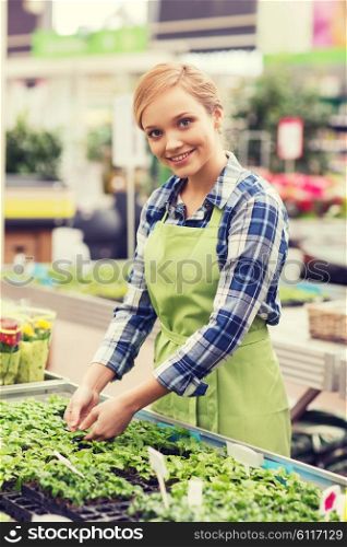 people, gardening and profession concept - happy woman or gardener taking care of seedling in greenhouse