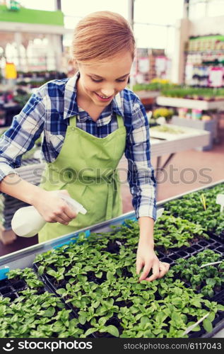 people, gardening and profession concept - happy woman or gardener with sprayer and seedling in greenhouse