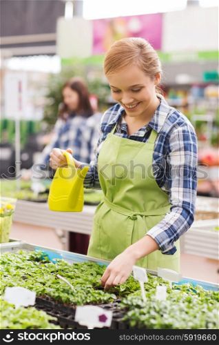 people, gardening and profession concept - happy woman or gardener with watering can and seedling in greenhouse