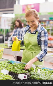 people, gardening and profession concept - happy woman or gardener with watering can and seedling in greenhouse