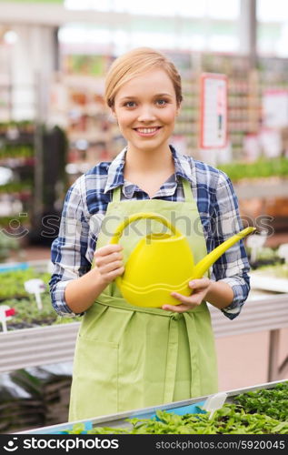 people, gardening and profession concept - happy woman or gardener with watering can and seedling in greenhouse