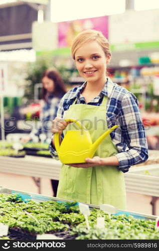 people, gardening and profession concept - happy woman or gardener with watering can and seedling in greenhouse