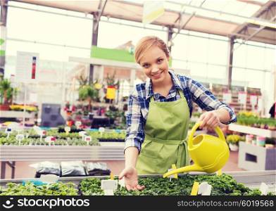 people, gardening and profession concept - happy woman or gardener with watering can and seedling in greenhouse
