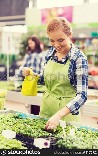 people, gardening and profession concept - happy woman or gardener with watering can and seedling in greenhouse