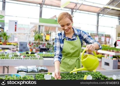 people, gardening and profession concept - happy woman or gardener with watering can and seedling in greenhouse of flower shop