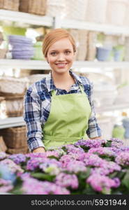 people, gardening and profession concept - happy woman with flowers in greenhouse