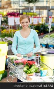 people, gardening, sale and consumerism concept -happy woman with shopping cart and flowers in shop or greenhouse