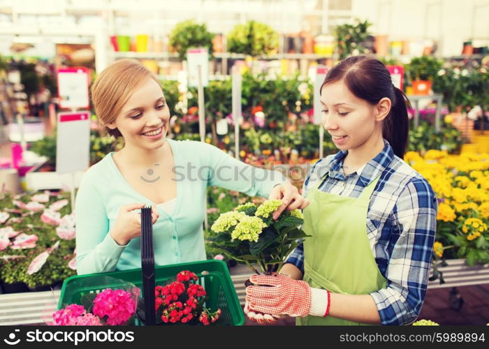 people, gardening, shopping, sale and consumerism concept - happy gardener helping woman with choosing flowers in greenhouse