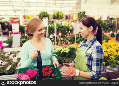 people, gardening, shopping, sale and consumerism concept - happy gardener helping woman with choosing flowers in greenhouse