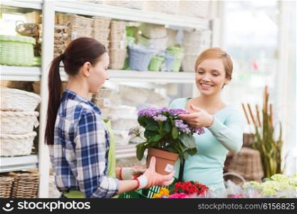 people, gardening, shopping, sale and consumerism concept - happy gardener helping woman with choosing flowers in greenhouse or shop