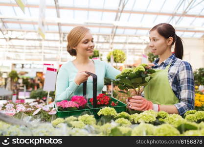 people, gardening, shopping, sale and consumerism concept - happy gardener helping woman with choosing flowers in greenhouse