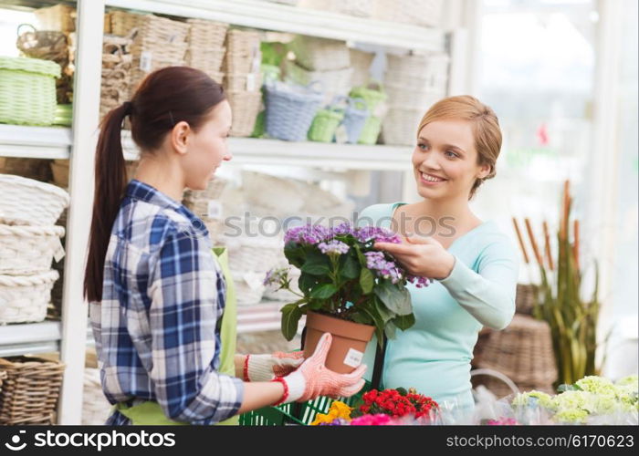 people, gardening, shopping, sale and consumerism concept - happy gardener helping woman with choosing flowers in greenhouse