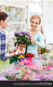 people, gardening, shopping, sale and consumerism concept - happy gardener helping woman with choosing flowers in greenhouse or shop