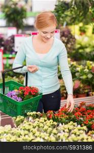 people, gardening, shopping, sale and consumerism concept - happy woman with basket choosing and buying flowers in greenhouse
