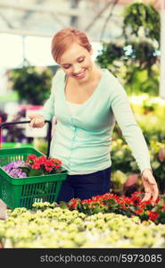 people, gardening, shopping, sale and consumerism concept - happy woman with basket choosing and buying flowers in greenhouse