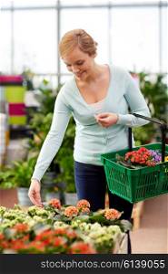 people, gardening, shopping, sale and consumerism concept - happy woman with basket choosing flowers in greenhouse or shop