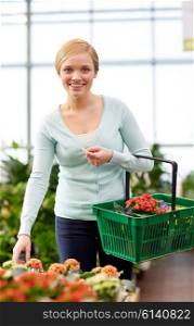people, gardening, shopping, sale and consumerism concept - happy woman with basket choosing flowers in greenhouse or shop