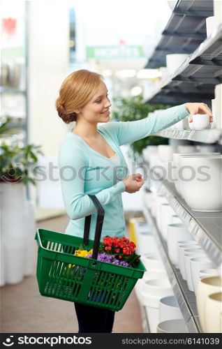 people, gardening, shopping, sale and consumerism concept - happy woman with basket choosing flower pot in shop