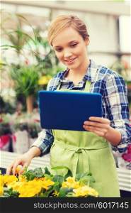 people, gardening, technology and profession concept - happy woman or gardener with tablet pc computer and flowers in greenhouse