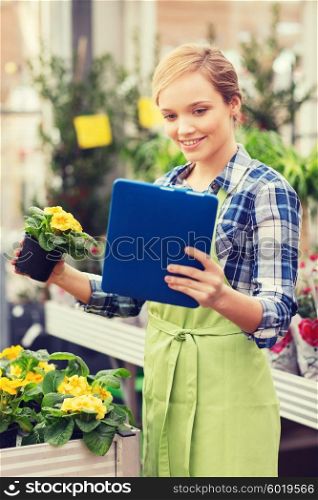 people, gardening, technology and profession concept - happy woman or gardener with tablet pc computer and flowers in greenhouse