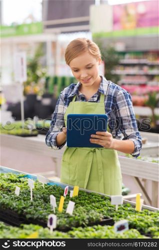 people, gardening, technology and profession concept - happy woman or gardener with tablet pc computer and seedling in greenhouse