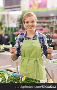 people, gardening tools and profession concept - happy woman or gardener with trowel and fork in greenhouse