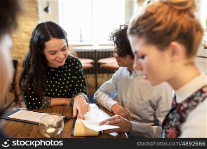 people, gathering and friendship concept - happy friends reading menu at restaurant