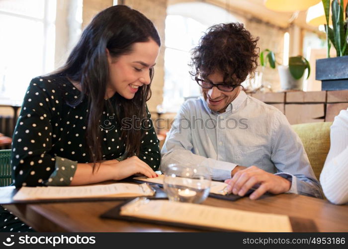 people, gathering and friendship concept - happy friends reading menu at restaurant. happy friends looking to menu at restaurant