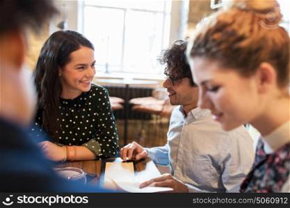 people, gathering and friendship concept - happy friends reading menu at restaurant. happy friends looking to menu at restaurant