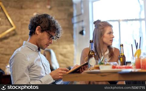 people, gathering and friendship concept - happy friends reading menu at restaurant. happy friends looking to menu at restaurant