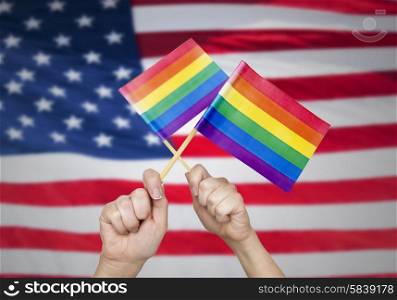 people, gay pride and homosexual concept - human hands holding rainbow flags over american flag background