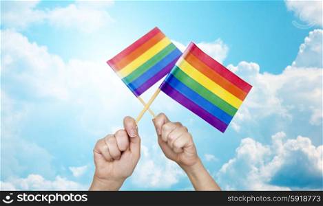 people, gay pride and homosexual concept - human hands holding rainbow flags over blue sky background