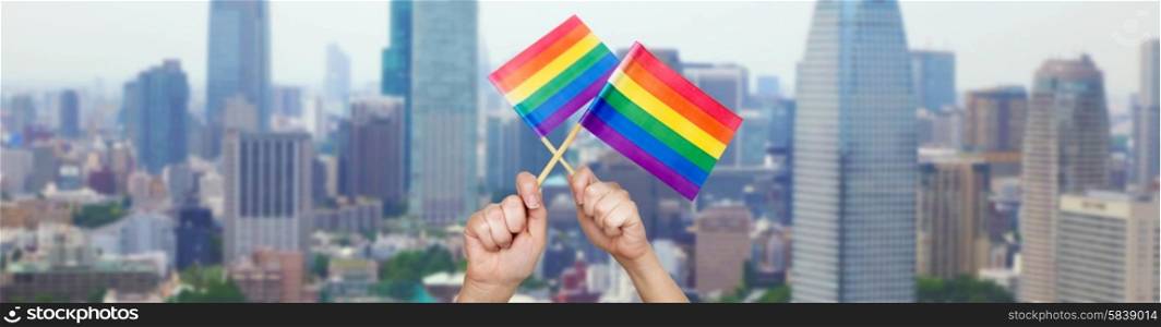 people, gay pride and homosexual concept - human hands holding rainbow flags over city background