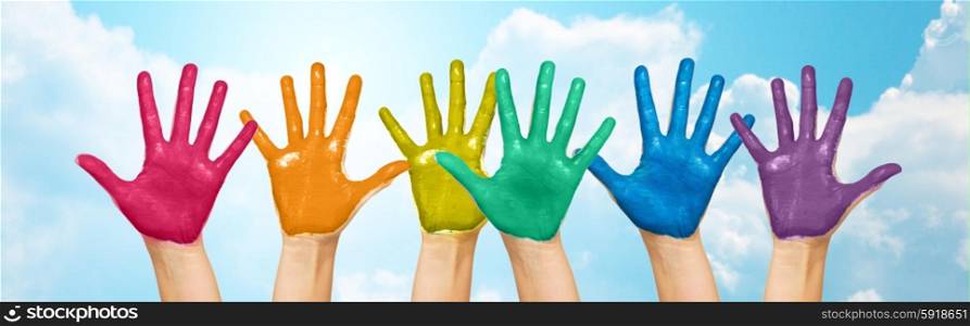 people, gay pride, creativity and art concept - palms of human hands painted in rainbow colors over blue sky and clouds background