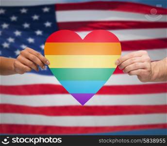 people, gay pride, gesture and homosexual concept - close up of couple hands holding rainbow heart shape over american flag background