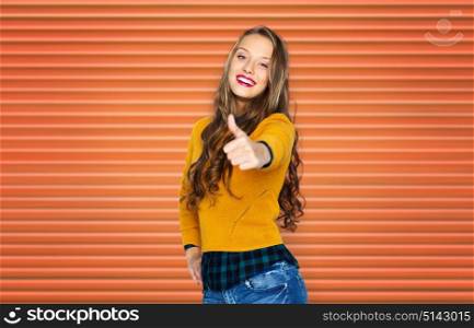 people, gesture and fashion concept - happy young woman or teen girl in casual clothes showing thumbs up over orange ribbed wall background. happy young woman or teen girl showing thumbs up