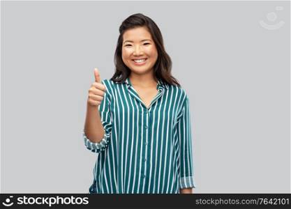 people, gesture and portrait concept - happy asian young woman showing thumbs up over grey background. happy asian woman showing thumbs up over grey