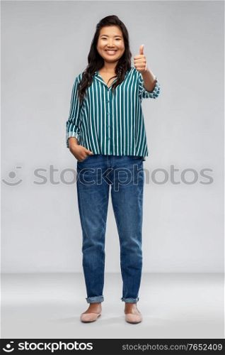 people, gesture and portrait concept - happy smiling asian young woman showing thumbs up over grey background. happy smiling asian woman showing thumbs up