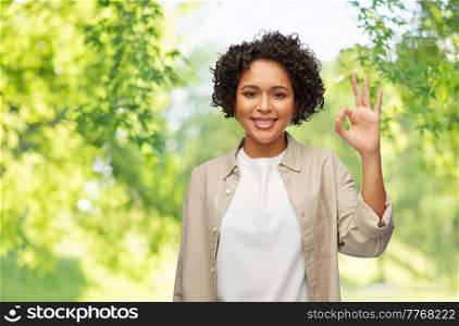 people, gesture and portrait concept - happy smiling woman in shirt showing ok hand sign over green natural background. portrait of woman in shirt showing ok gesture