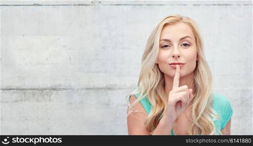 people, gesture and secret concept - beautiful young woman holding finger at her lips over gray concrete wall background