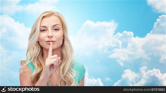 people, gesture and secret concept - beautiful young woman holding finger at her lips over blue sky and clouds background