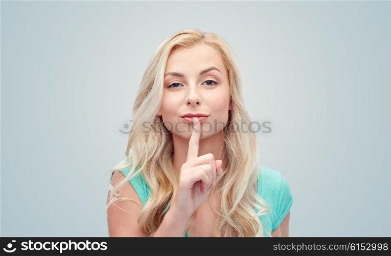 people, gesture and secret concept - beautiful young woman holding finger at her lips over gray background