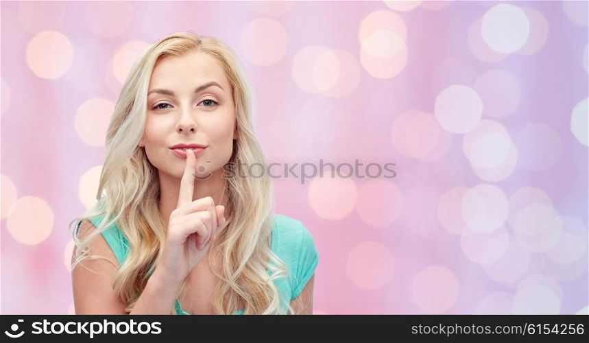 people, gesture and secret concept - beautiful young woman holding finger at her lips over pink holidays lights background